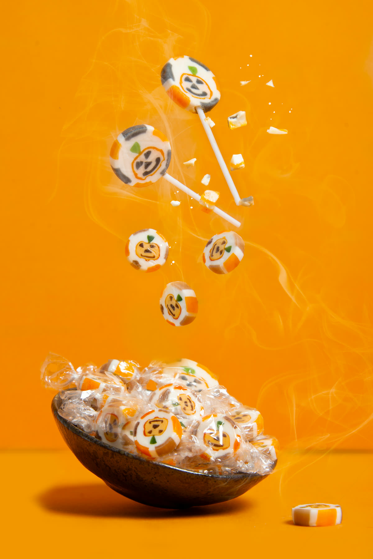 Sucettes d'Halloween en lévitation au-dessus d'un bol, fond orange et fumée