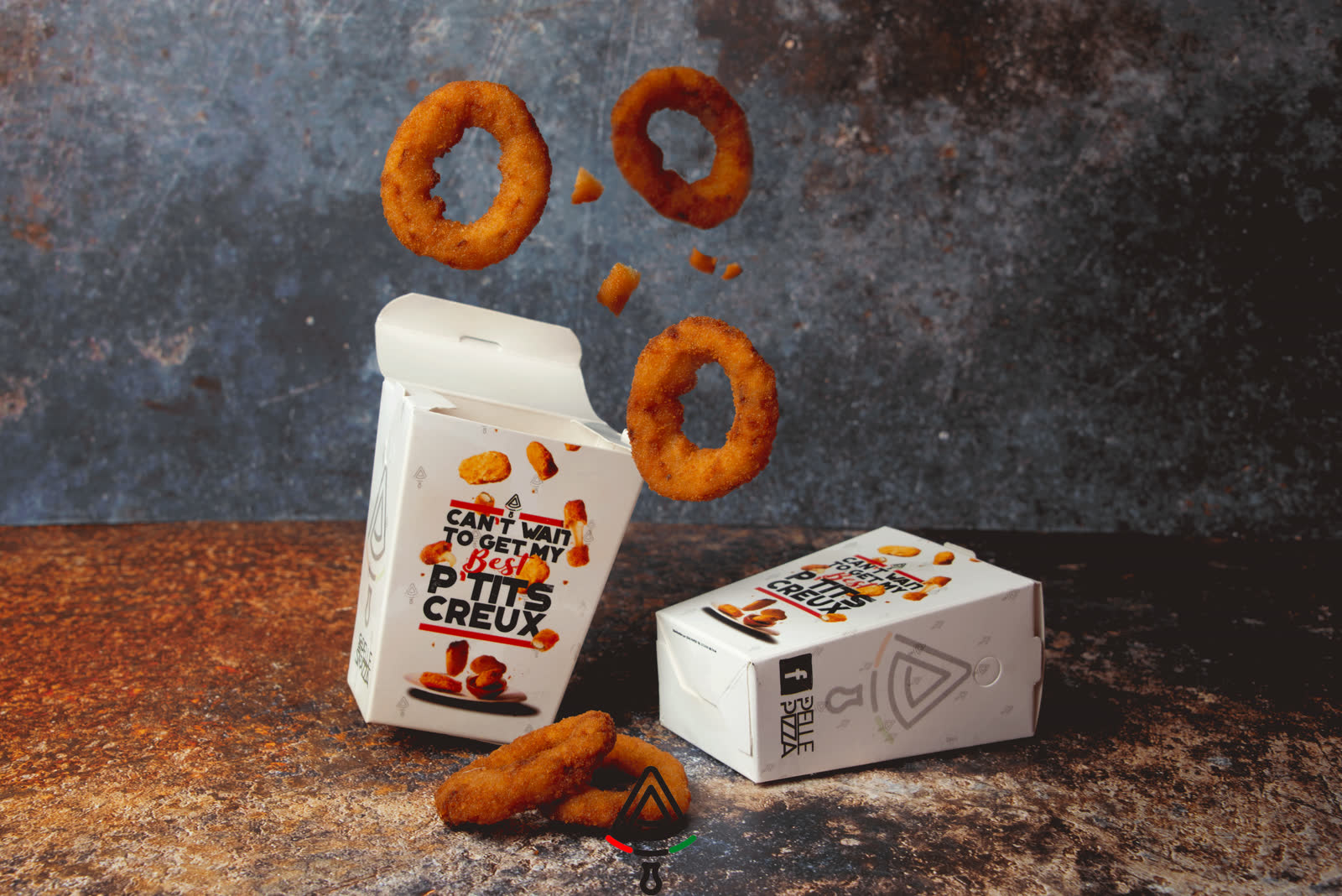 Onion rings en lévitation au-dessus de leurs boîtes en carton, sur fond ardoise