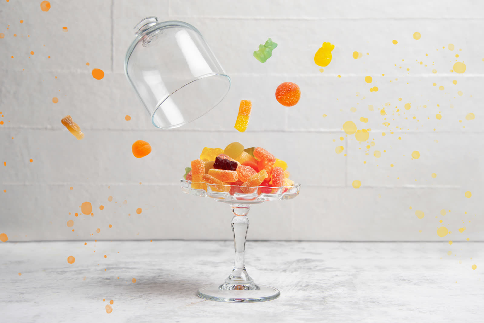 Bonbons gélifiés colorés sur un présentoir en verre, cloche en lévitation et éclaboussures de couleur