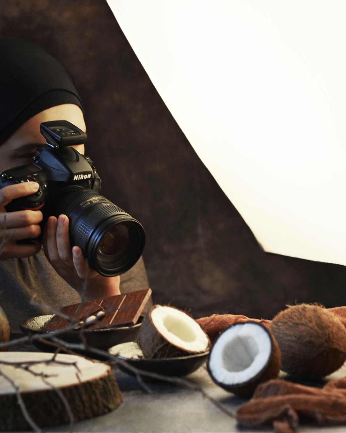 Mélia Lehlou en studio, appareil photo à l'œil, face à une mise en scène de noix de coco et de chocolat